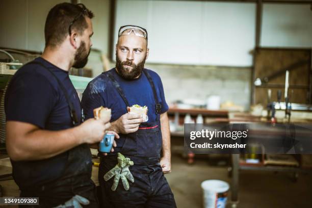 manual workers talking while eating sandwiches on a break in a workshop. - snickare bildbanksfoton och bilder