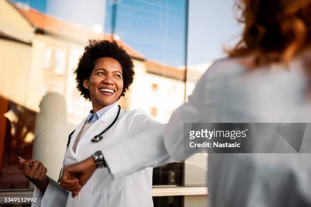 elbow bumping while standing in front of the hospital - elbow bump stock pictures, royalty-free photos & images