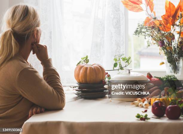 woman sitting at table with pumpkin, various vegetables, cooking pot and autumn bouquet at window background - fall bouquet stock pictures, royalty-free photos & images