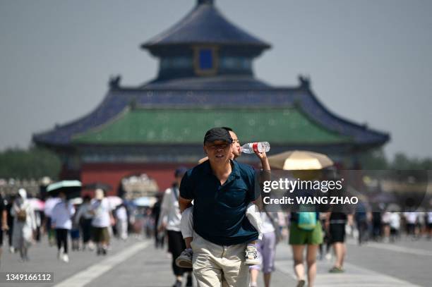 Man carries a child drinking water at the Temple of Heaven on a hot day in Beijing on June 30, 2023.