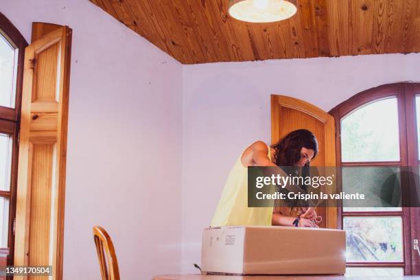 young woman opening a cardboard package at home - online shopping opening package stockfoto's en -beelden