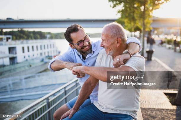 senior man with his mature son embracing outdoors in town. - fist bump photos et images de collection