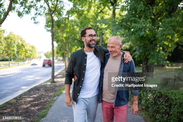 senior man with his mature son embracing outdoors in park. - hand auf der schulter stock-fotos und bilder