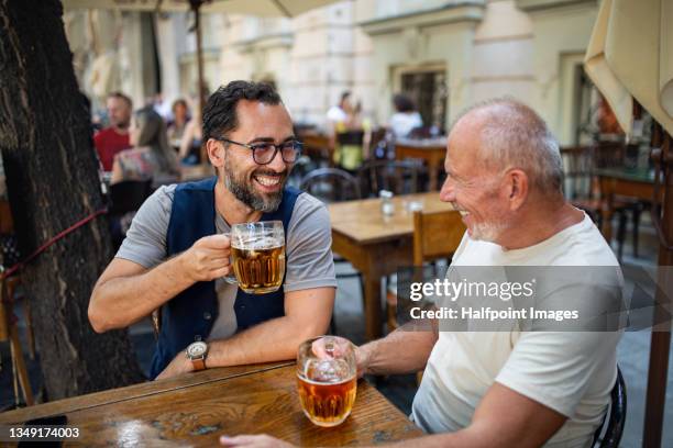 senior man with his mature son drinking beer outdoors in pub. - man sipping beer smiling stockfoto's en -beelden