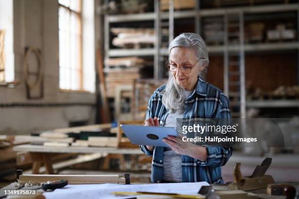senior female carpenter using tablet in carpentry workshop. - kleinunternehmen stock-fotos und bilder