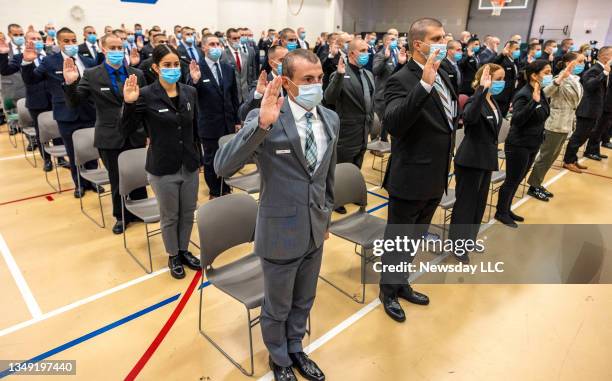 Suffolk County police recruits wear masks as they take the oath during a swearing-in ceremony at the department's police academy on the grounds of...