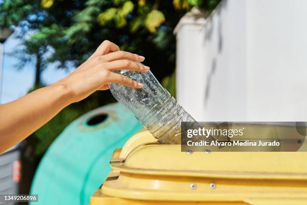 close up shot of a hand throwing a used plastic bottle into the yellow garbage can for recycling. - recycling fotografías e imágenes de stock