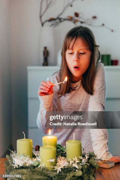 young girl lighting the first candle on advent wreath and blowing the safety match out. - advent wreath stock pictures, royalty-free photos & images