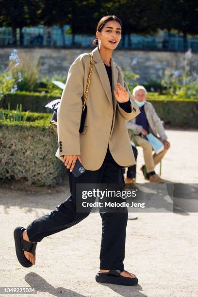 Model Nora Attal waves and wears a tan blazer, Alexander McQueen bag, black pants, and black chunky platform sandals after the Dior show on September...