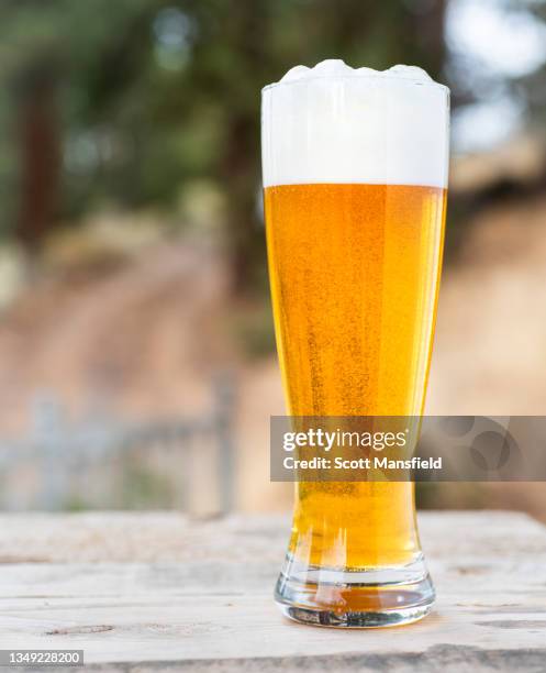 side view of a foamy glass of light beer on an outdoor table - wheat beer stock pictures, royalty-free photos & images