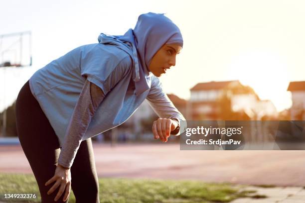 modern muslim sportswoman checking her pulse trace on a fitness tracker - exhausted runner stock pictures, royalty-free photos & images