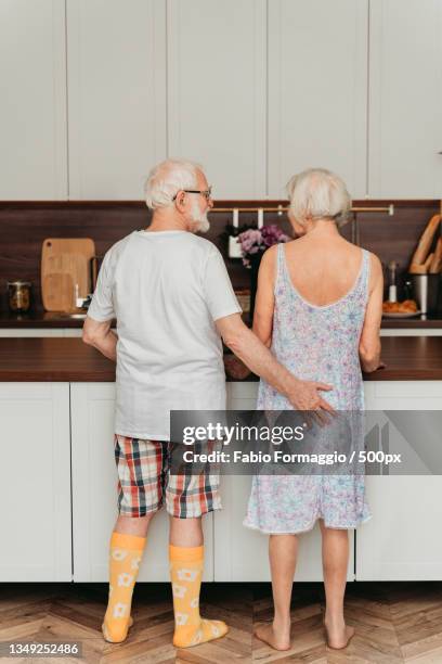 rear view of senior couple standing in kitchen at home - vieilles fesses photos et images de collection