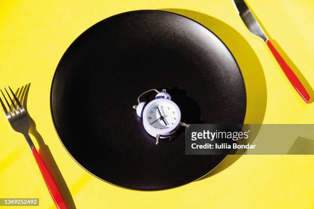 clock alarm on the plate with cutlery on yellow background - fasten stock-fotos und bilder
