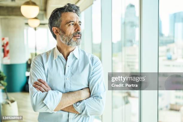 nachdenklicher geschäftsmann schaut durch das bürofenster - mittelalter mann stock-fotos und bilder