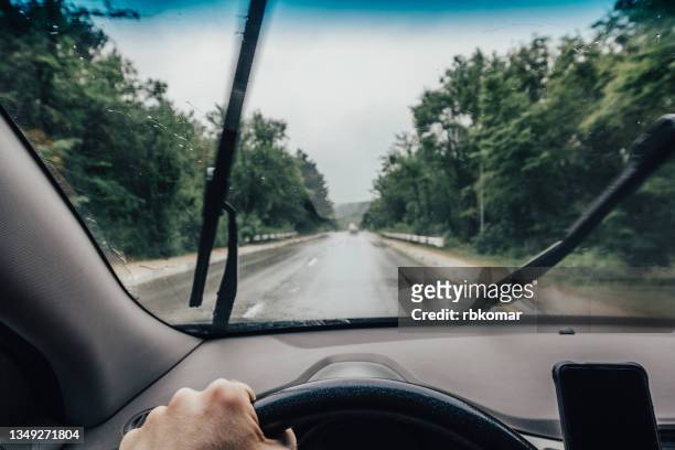 the driver's hand holds the steering wheel while it is raining heavily - parabrisas fotografías e imágenes de stock