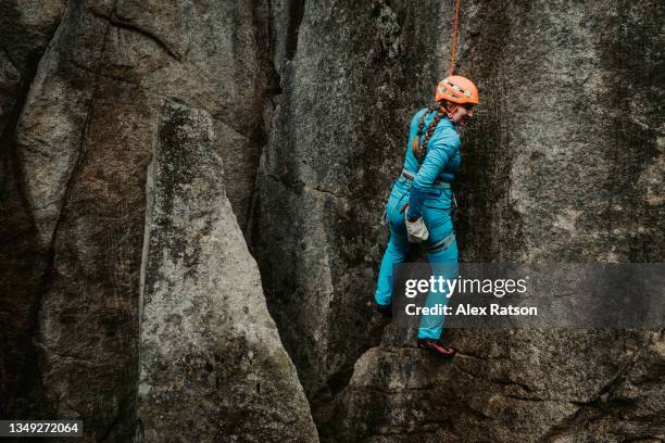female rock climber wearing all blue rock climbs on a dark and moody day - rock face stock pictures, royalty-free photos & images