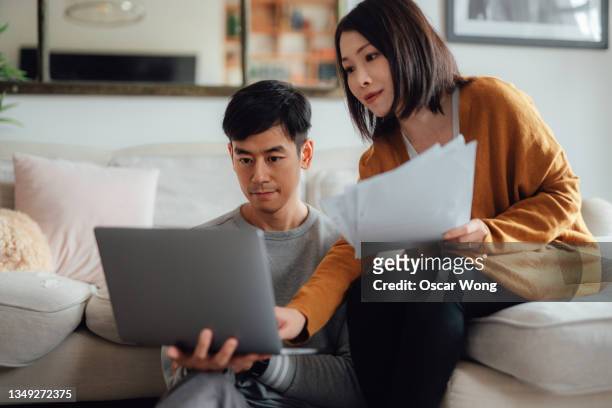 young couple discussing over financial bills while using laptop on sofa - schulden stock-fotos und bilder