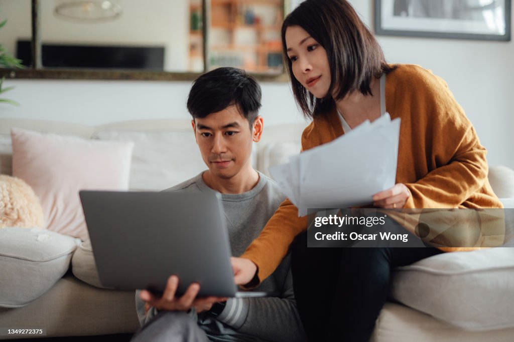 Young couple discussing over financial bills while using laptop on sofa
