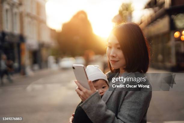 woman with toddler ordering taxi using mobile app on smartphone in city - babytrage stock-fotos und bilder