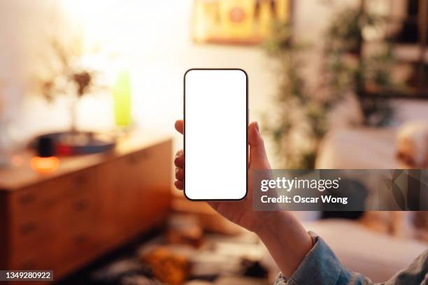 mockup image of woman holding smartphone with blank white screen at living room - iphone mockup stock pictures, royalty-free photos & images