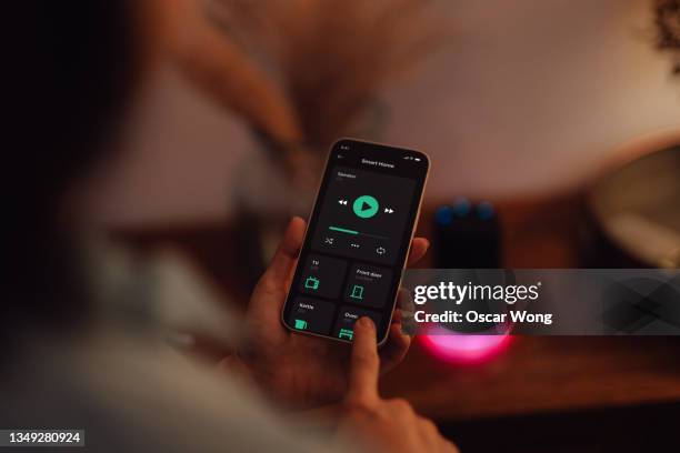 young woman using smartphone to control smart speaker of a modern smart home - woman looking over shoulder stock-fotos und bilder