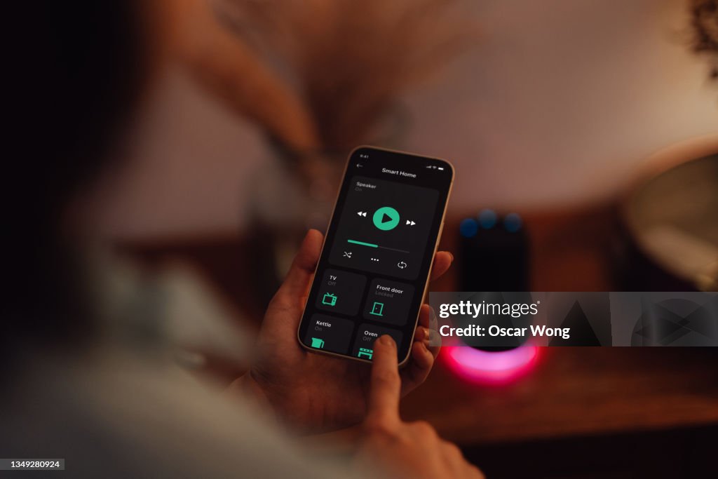 Young woman using smartphone to control smart speaker of a modern smart home