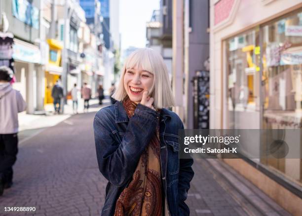 young woman with platinum blonde hair walking on shopping street with smile - harajuku district stock pictures, royalty-free photos & images