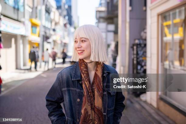 junge frau mit platinblonden haaren, die mit einem lächeln auf der einkaufsstraße spazieren geht - street fashion japan stock-fotos und bilder