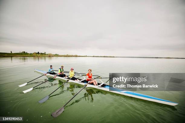 wide shot of smiling female crew preparing to row quad scull during early morning workout - remo con espadilla fotografías e imágenes de stock