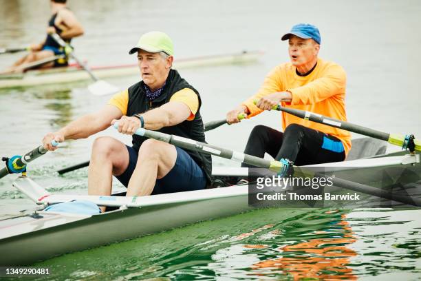 medium wide shot of senior male rowers rowing double scull during early morning workout - taking a shot - sport imagens e fotografias de stock