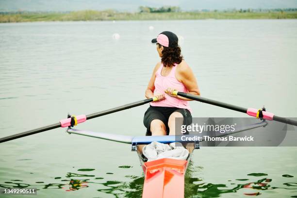 medium wide shot of mature female rower looking over shoulder while rowing single scull during workout - single scull stockfoto's en -beelden