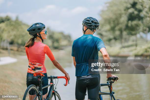 rear view asian chinese couple cyclist taking a break walking with road bike during weekend morning together at river bank looking away - cycling vest stock pictures, royalty-free photos & images