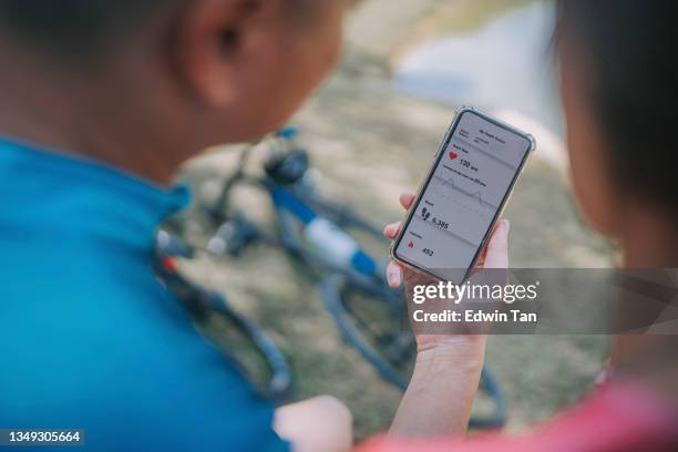 sopra la spalla coppia cinese asiatica che controlla il fitness tracker confrontando l'app mobile sui dati e sui risultati dell'esercizio mattutino - inseguire foto e immagini stock