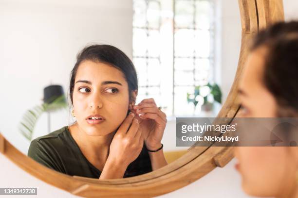 mujer joven poniéndose pendientes en un espejo en casa - earring fotografías e imágenes de stock