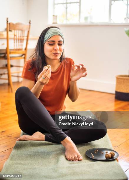 smiling young woman eating a healthy snack after a home yoga session - snack break stock pictures, royalty-free photos & images