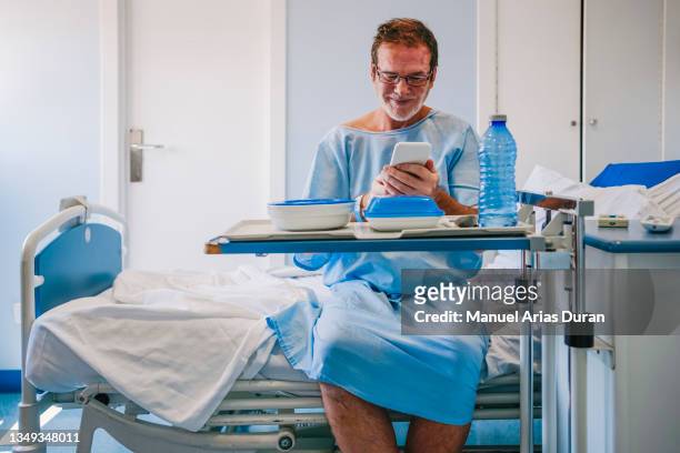 sick sitting in a hospital bed, with hospital food. receiving a positive phone call - cellphone cancer illness stock pictures, royalty-free photos & images