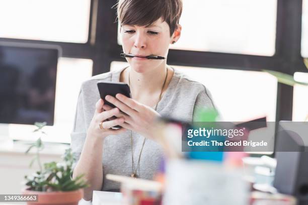 businesswoman text messaging on smart phone at desk - métier du design photos et images de collection