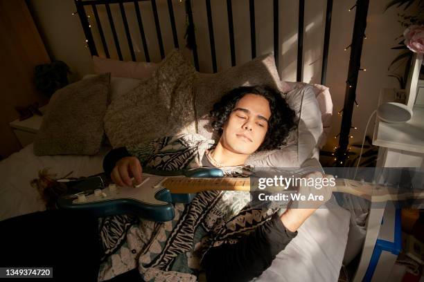 young man lies on his bed while playing the guitar - masculinidad moderna fotografías e imágenes de stock