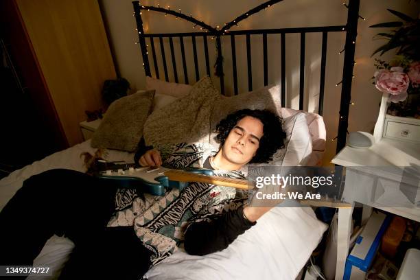 young man lies on his bed while playing the guitar - guitar photos et images de collection