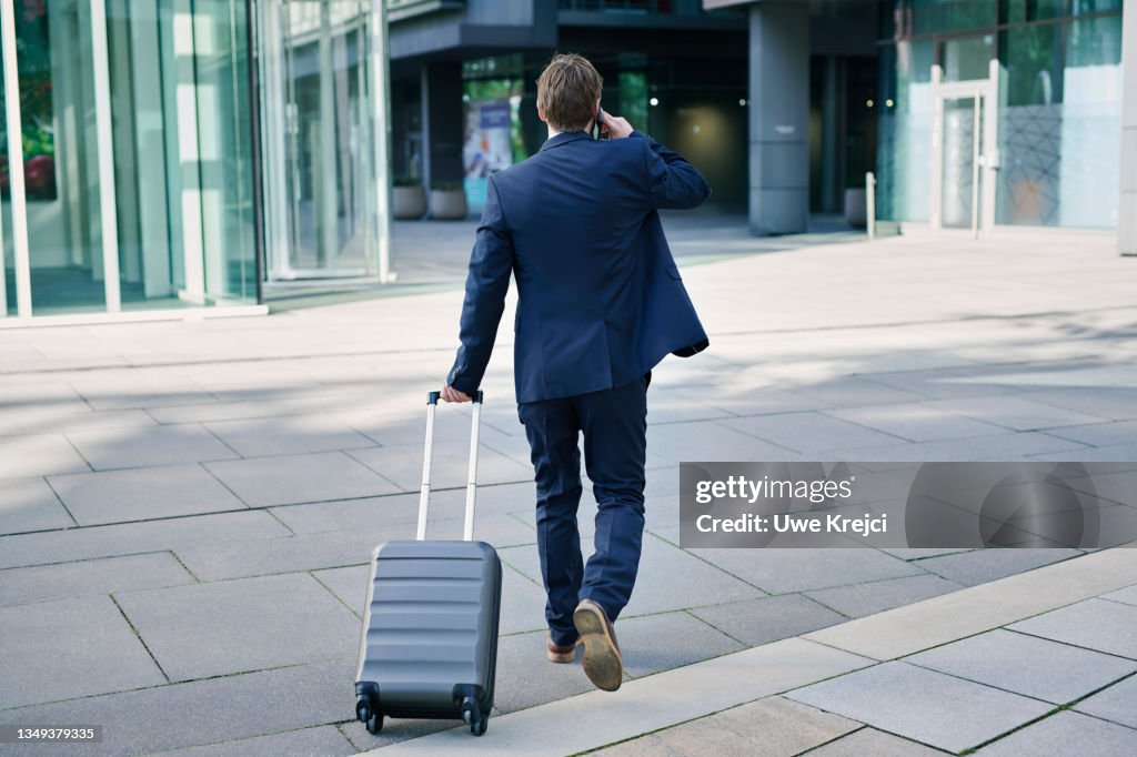 Business man with phone and suitcase walking towards building