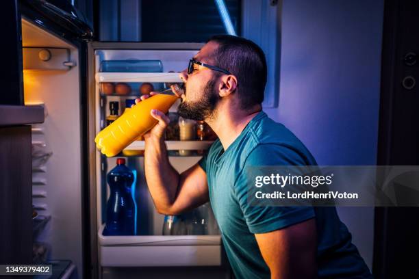 mann trinkt saft vor dem kühlschrank - ungesund leben stock-fotos und bilder