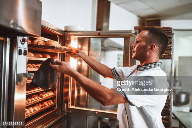 männlicher bäcker überprüft den zustand des frischen gebäcks im ofen - baker man stock-fotos und bilder