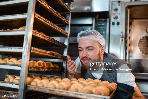 let's enjoy the smell - male baker smelling croissants fresh out of oven - baker smelling bread stockfoto's en -beelden