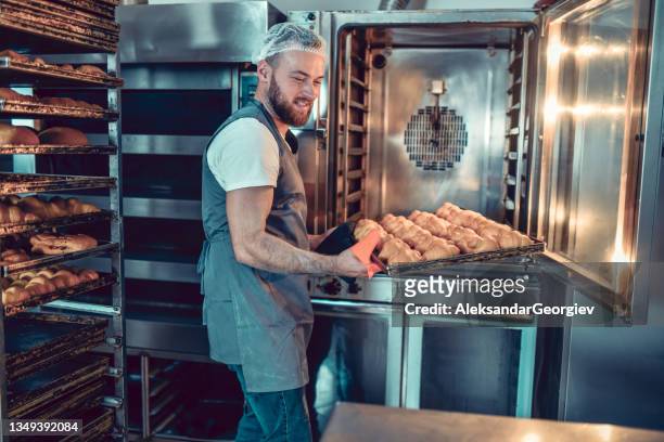 smiling bearded baker taking out croissants before burning in oven - bakery 個照片及圖片檔