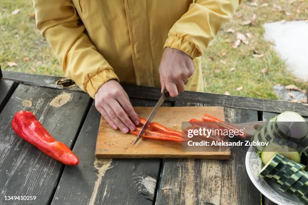 a woman in a bright yellow jacket slices zucchini and bell peppers to cook them on the grill, on an autumn sunny day. vacation or vacation in a country house, on a picnic or camping. you cook on coals, on fire, by yourself. - red pepper stock pictures, royalty-free photos & images