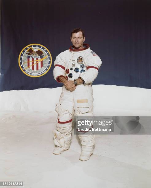 Portrait of Astronaut John W Young, Apollo 16 Mission Commander, wearing a spacesuit, posing next to the Apollo 16 insignia.