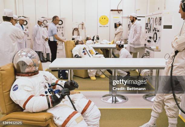 The Apollo 16 astronauts undergo prelaunch spacesuit pressure checks in the Manned Spacecraft Operation Building. Seated from front to rear are: John...