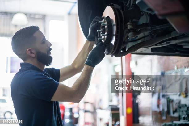 joven mecánico revisando el disco de freno de un coche en ascensor en el taller - car brakes fotografías e imágenes de stock