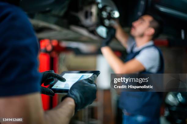 focus on foreground of engineer holding a tablet checking the readings of the carâs sensor while the mechanic adjusts them on the disk - command and control bildbanksfoton och bilder