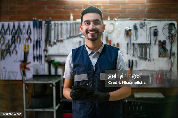 freundlicher geschäftsinhaber seiner garagenwerkstatt, der ein tablet hält, während er sehr fröhlich vor der kamera steht - seleccion colombia stock-fotos und bilder